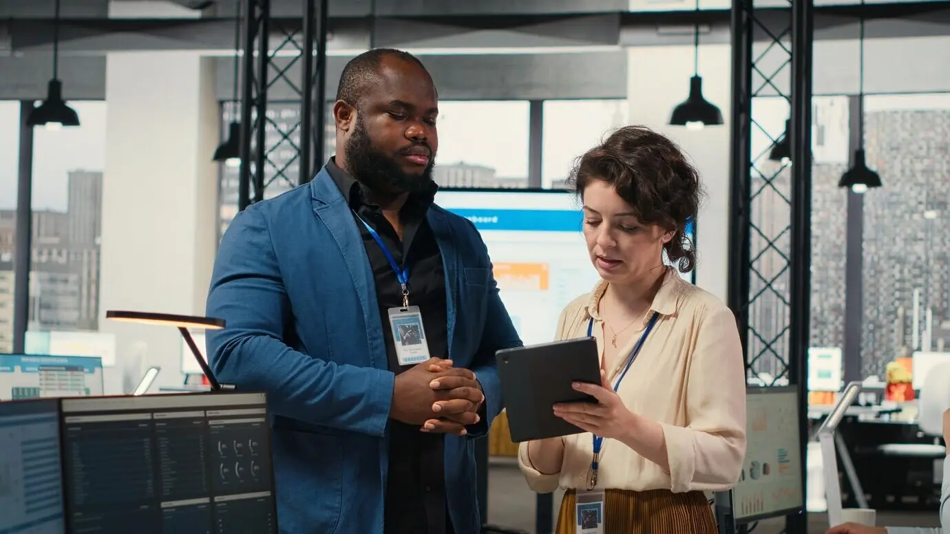 Zwei Mitarbeitende prüfen Dateneinblicke auf einem Tablet in einem professionellen Arbeitsumfeld im Rahmen der Geschäftsentwicklung.